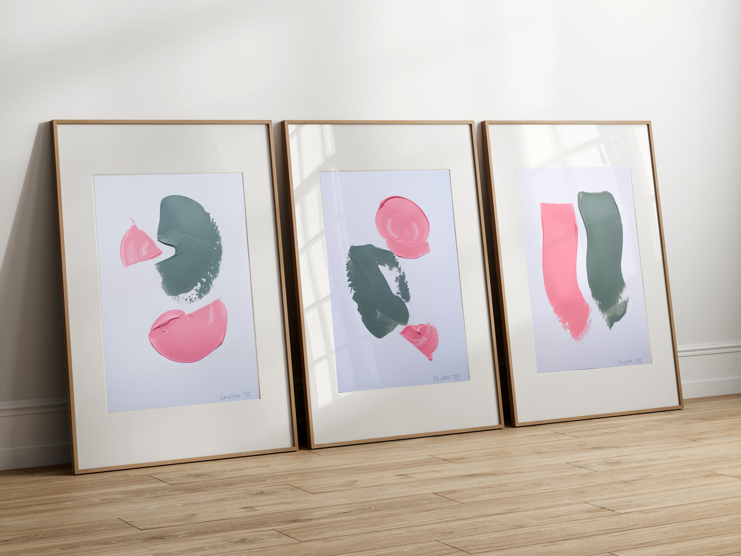 Three framed abstract art prints on a wooden floor against a white wall.